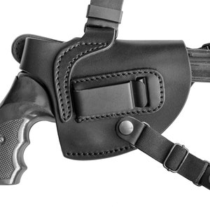 May include: A black leather shoulder holster with a black revolver inside. The holster has a strap that goes over the shoulder and a clip that attaches to the belt.