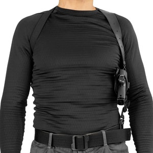 May include: A black leather shoulder holster with a black handgun. The holster is worn over a black long-sleeved shirt and a black belt.