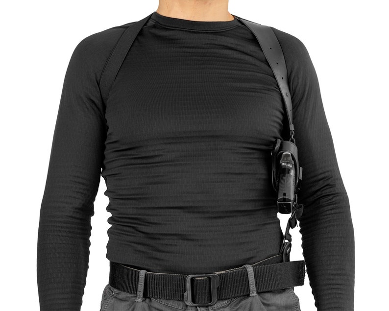 May include: A black leather shoulder holster with a black handgun. The holster is worn over a black long-sleeved shirt and a black belt.