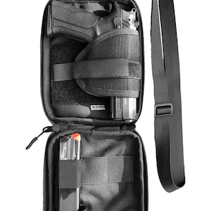 Könnte beinhalten: Schwarze Nylon-Umhängetasche mit Reißverschluss. Die Tasche hat ein integriertes Holster für eine Pistole und ein separates Fach für ein Magazin. Die Tasche ist offen und das Holster ist leer.
