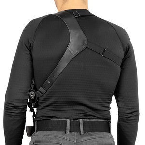 May include: A black leather shoulder holster with an adjustable strap. The holster is worn over a black long-sleeved shirt and a black belt.