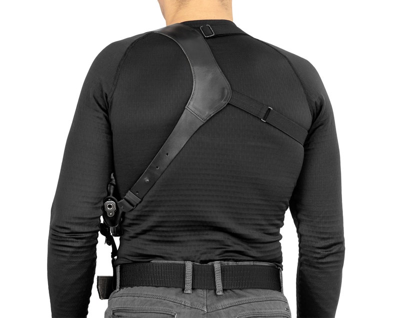 May include: A black leather shoulder holster with an adjustable strap. The holster is worn over a black long-sleeved shirt and a black belt.