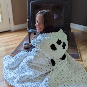 Puede incluir: Una manta con capucha blanca y negra con un dise&ntilde;o de oso panda. La manta est&aacute; hecha de un material suave y afelpado y presenta manchas negras en la capucha. La manta est&aacute; dise&ntilde;ada para ser usada y proporciona calidez y comodidad.