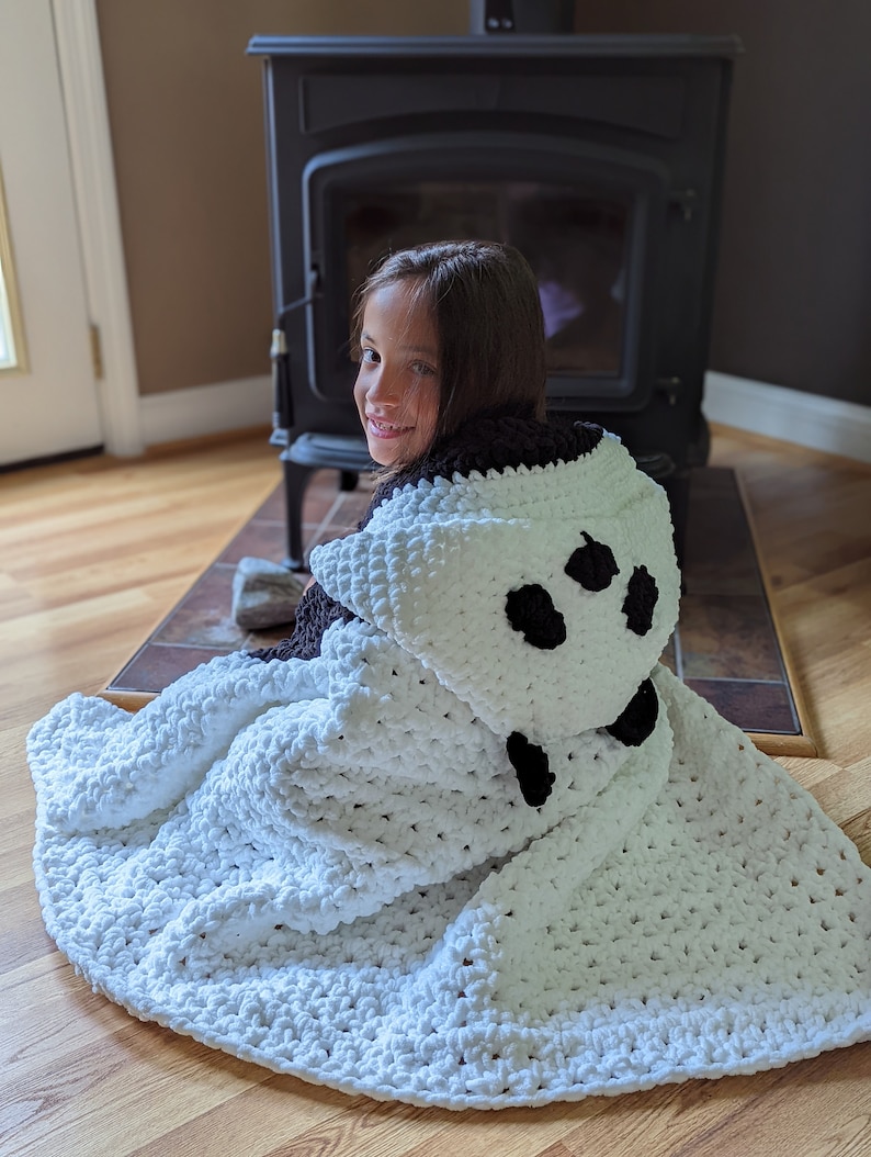 Puede incluir: Una manta con capucha blanca y negra con un dise&ntilde;o de oso panda. La manta est&aacute; hecha de un material suave y afelpado y presenta manchas negras en la capucha. La manta est&aacute; dise&ntilde;ada para ser usada y proporciona calidez y comodidad.