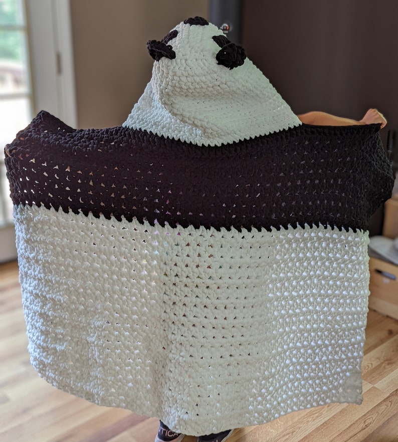 Puede incluir: Una manta con capucha de oso panda hecha a mano. La manta es blanca con una banda y capucha marr&oacute;n oscuro, con orejas y ojos negros. Hecha de un material suave y texturizado, ideal para la comodidad.