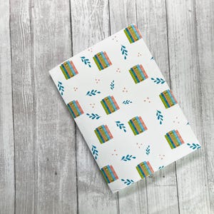 May include: White wrapping paper with a repeating pattern of stacked books, green leaves, and pink dots.