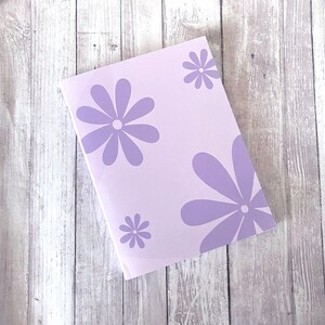 May include: A lavender notebook with a floral design featuring purple flowers on a white background.