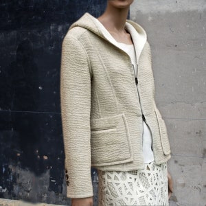 Può includere: Una giacca con cappuccio color crema con chiusura a zip e due tasche. La giacca è realizzata in tessuto strutturato e ha una vestibilità rilassata.