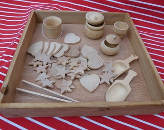 May include: A wooden tray filled with various wooden shapes and containers. Includes stars, hearts, small buckets, bowls, scoops, and tongs. The items are made of light-colored wood and are arranged on a wooden surface.