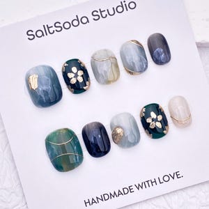 May include: A set of ten press-on nails on a white display card labeled SaltSoda Studio and HANDMADE WITH LOVE. The nails feature a mix of dark green, grey, and cream marble patterns, gold foil floral accents, and thin gold wire line details.