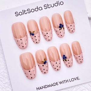 May include: A set of ten press-on nails on a white display card labeled SaltSoda Studio and HANDMADE WITH LOVE. The nails feature a nude base with a French tip design, black polka dots, and small blue berry accents with green leaves on select nails.