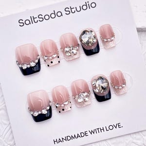 May include: A set of false nails with a French manicure design. The nails have a pale pink base, black tips, and are decorated with rhinestones and glitter. The card reads "SaltSoda Studio" and "HANDMADE WITH LOVE."