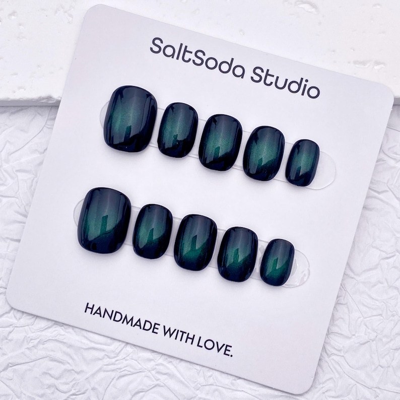 May include: A set of dark teal press-on nails with a glossy finish. The nails are arranged on a white card with the text "SaltSoda Studio" and "HANDMADE WITH LOVE."