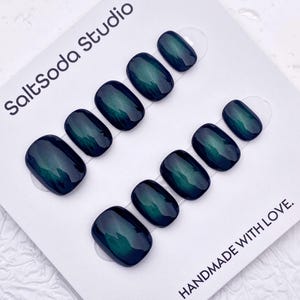 May include: Oval-shaped, dark teal press-on nails arranged in two rows on a white card. The nails have a glossy finish and a subtle color gradient. The card has the text "SaltSoda Studio" and "HANDMADE WITH LOVE."