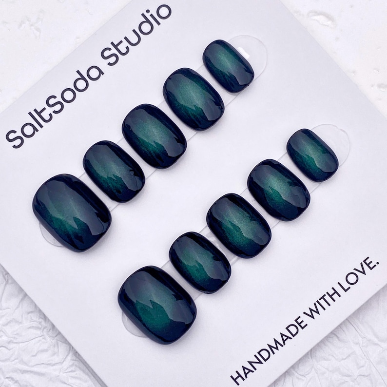 May include: Oval-shaped, dark teal press-on nails arranged in two rows on a white card. The nails have a glossy finish and a subtle color gradient. The card has the text "SaltSoda Studio" and "HANDMADE WITH LOVE."