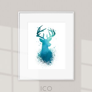 Puede incluir: Una impresión en acuarela enmarcada con una silueta de ciervo turquesa con cuernos detallados. El ciervo se encuentra sobre un fondo blanco con un efecto de salpicaduras. La impresión está en un marco blanco. El texto "ICONIC watercolors" está en la parte inferior.