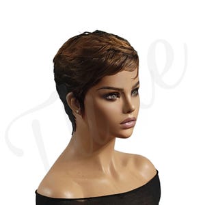 May include: A short, brown and blonde pixie cut wig with a side part. The wig is styled with a textured, choppy look.