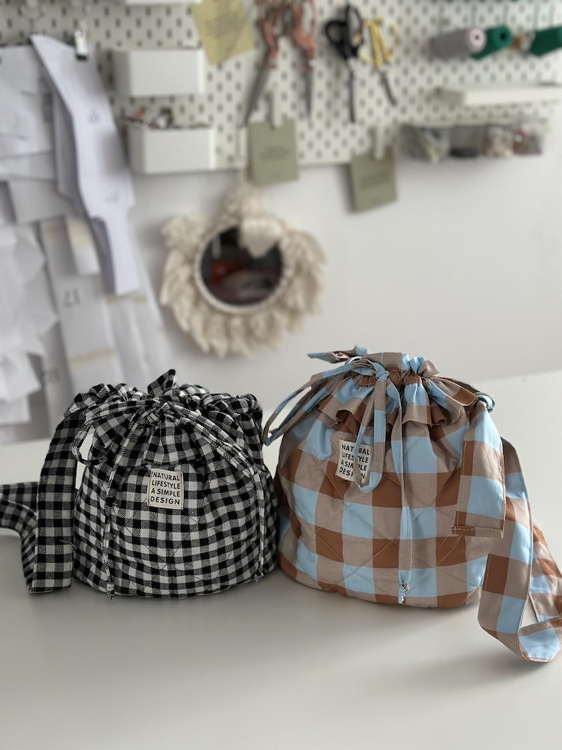 K&ouml;nnte beinhalten: Zwei Kordelzugbeutel auf einer wei&szlig;en Oberfl&auml;che. Einer ist schwarz-wei&szlig;-kariert, der andere braun, blau und beige kariert. Beide Beutel haben ein Etikett mit der Aufschrift "NATURAL LIFESTYLE A SIMPLE DESIGN".