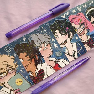 May include: A collection of character art cards featuring anime-style illustrations, with two purple pens. The cards showcase various characters with unique hairstyles and expressions, set against a starry background. The pens are a vibrant purple color.