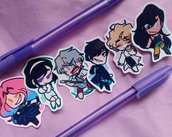 Pode incluir: Uma vista superior de canetas roxas e adesivos de personagens de desenhos animados em uma superfície lavanda. Os adesivos retratam personagens de estilo anime com diferentes cores de cabelo e roupas. As canetas são roxas.