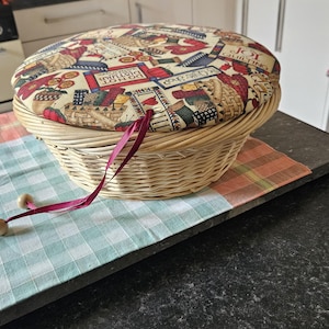 May include: A wicker basket with a fabric lid featuring a colourful patchwork design with the words "Joy of Quilting", "Do Not Disturb", and "Sewing Shop". The basket has a red ribbon tied around the handle.