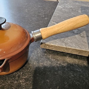 May include: A brown cast iron saucepan with a wooden handle and a lid. The saucepan has a spout on the side.