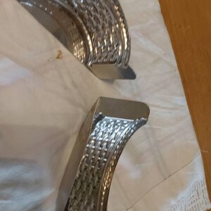 May include: Two silver metal molds with a woven pattern. The molds are shaped like half circles and are lying on a white surface.