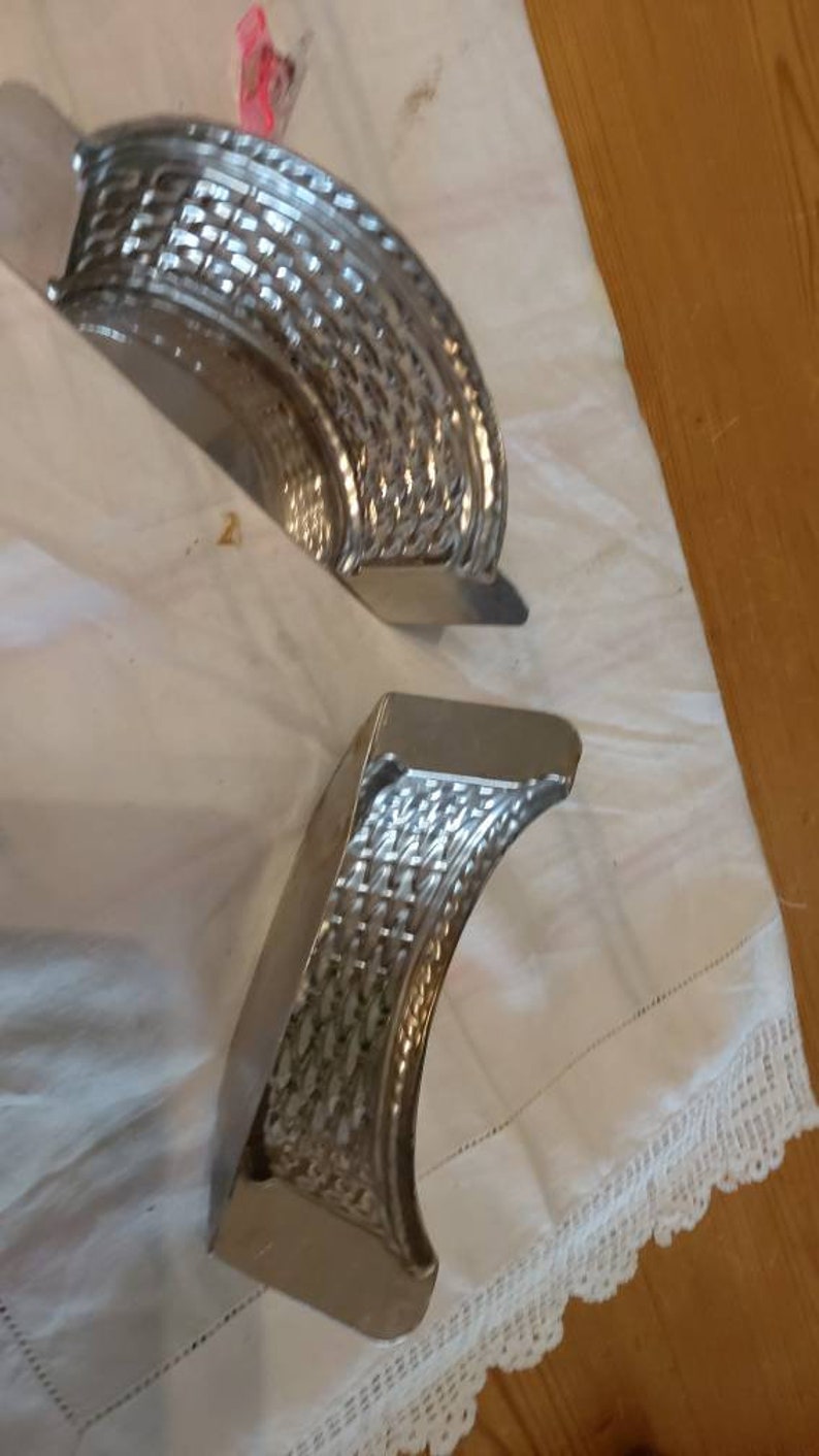 May include: Two silver metal molds with a woven pattern. The molds are shaped like half circles and are lying on a white surface.
