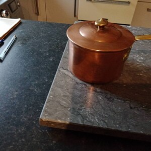 May include: A copper saucepan with a brass handle and lid. The saucepan is sitting on a grey countertop.