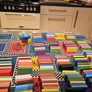 May include: A table covered in a black and white chequered tablecloth with colourful wooden blocks stacked in rows. The blocks are arranged in a variety of colours, including red, blue, green, yellow, and purple.