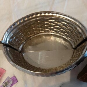 May include: A silver metal mold shaped like a basket with a woven pattern. The mold is open and the inside is visible. The mold is sitting on a white surface.
