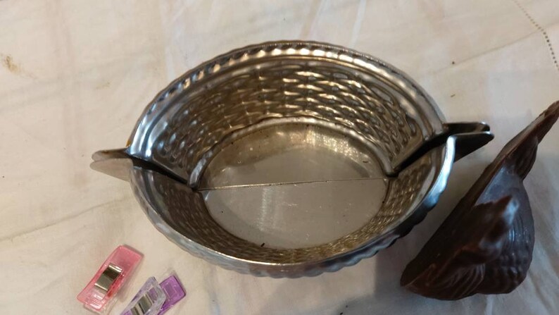 May include: A silver metal mold shaped like a basket with a woven pattern. The mold is open and the inside is visible. The mold is sitting on a white surface.