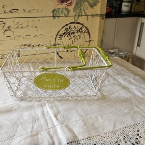 May include: White wire basket with a green handle and a green label that says "Mon p'tit marche".