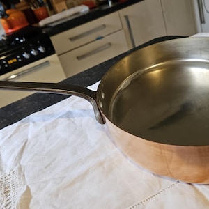 May include: A copper saucepan with a long handle. The saucepan is empty and has a shiny, reflective surface.