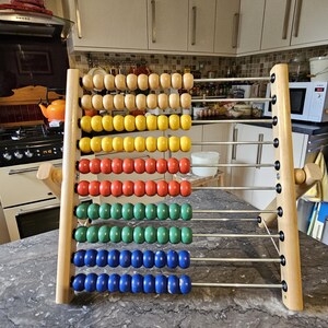 May include: A wooden abacus with colorful beads. The abacus has 10 rows of beads, each row with a different color: brown, yellow, red, green, and blue. The abacus is on a gray countertop.