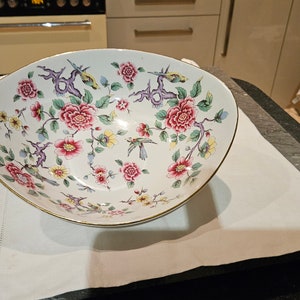 Könnte beinhalten: Eine weiße Keramikschüssel mit einem Blumendesign mit rosa, roten und gelben Blumen und grünen Blättern. Die Schüssel hat einen goldenen Rand und ein Vogeldesign.