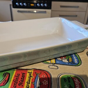 May include: A white ceramic baking dish with a light blue and green floral pattern. The dish is empty and has a rectangular shape.