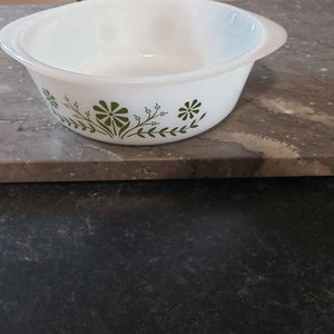 May include: White ceramic baking dish with a green floral design. The dish has a rounded shape and a slightly flared rim.