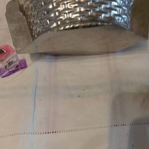 May include: A silver metal basket mold with a woven pattern. A small chocolate bunny figurine is on a white surface.