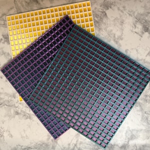 May include: Three square grid panels arranged in a stack. The top panel is teal with a dark interior, the middle panel is purple with a dark interior, and the bottom panel is yellow with a white interior. Each panel features a uniform grid pattern.