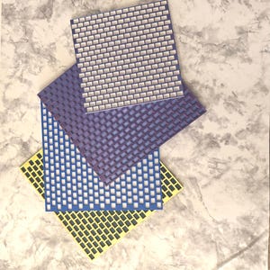 May include: Three square, flat, grid-patterned sheets stacked in a staggered arrangement. The top sheet is white with a purple grid, the middle sheet is purple with a blue grid, and the bottom sheet is yellow with a dark gray grid pattern.