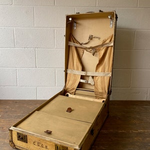 May include: An antique, tan leather suitcase with a C.G.C.E. label. The suitcase is open and has a built-in hanger and a removable tray.
