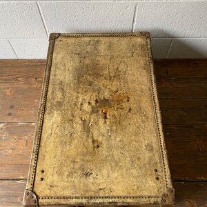 May include: A vintage leather suitcase with a worn, cream-colored exterior. The suitcase has brass hardware and a leather handle.