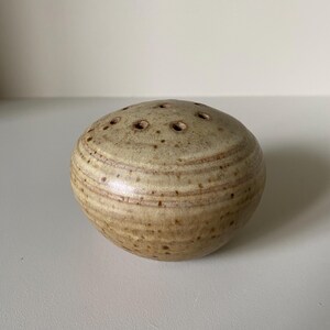 May include: A small, round, brown ceramic vase with a textured surface and multiple holes for flower stems.