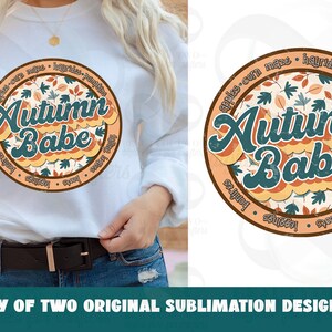 May include: A white sweatshirt with a round, orange and brown graphic design featuring the text "Autumn Babe" surrounded by fall-themed words like "apples", "corn", "hayrides", and "pumpkins".