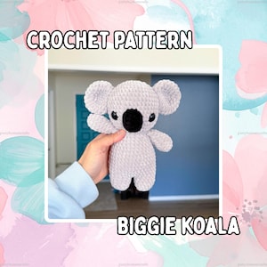 May include: A light gray crocheted koala plush toy with a large black nose and dark eyes. The text CROCHET PATTERN and BIGGIE KOALA is displayed in white letters with black outlines against a background of soft pink and blue watercolor flowers.