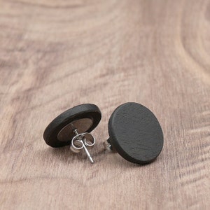 May include: A pair of black wooden stud earrings with silver posts. The earrings are round and have a smooth, matte finish.