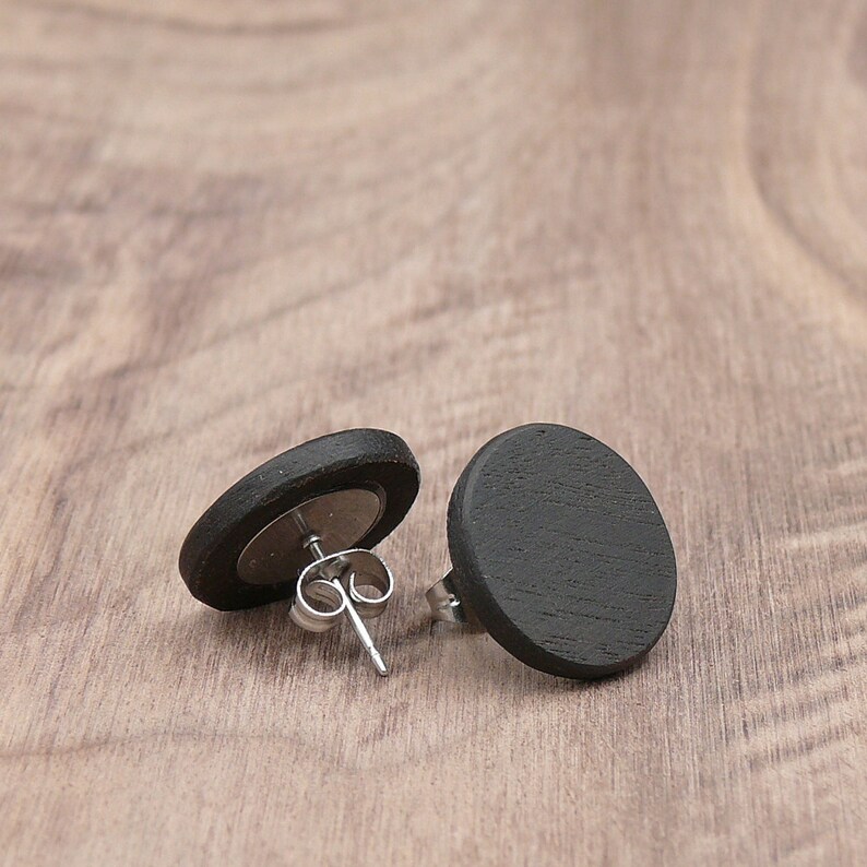 May include: A pair of black wooden stud earrings with silver posts. The earrings are round and have a smooth, matte finish.