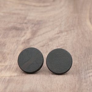 May include: A pair of black wooden earrings with a circular shape and a textured surface.