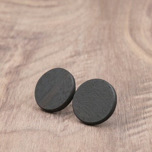 May include: Two black wooden circle earrings. The earrings are smooth and have a slightly textured surface.